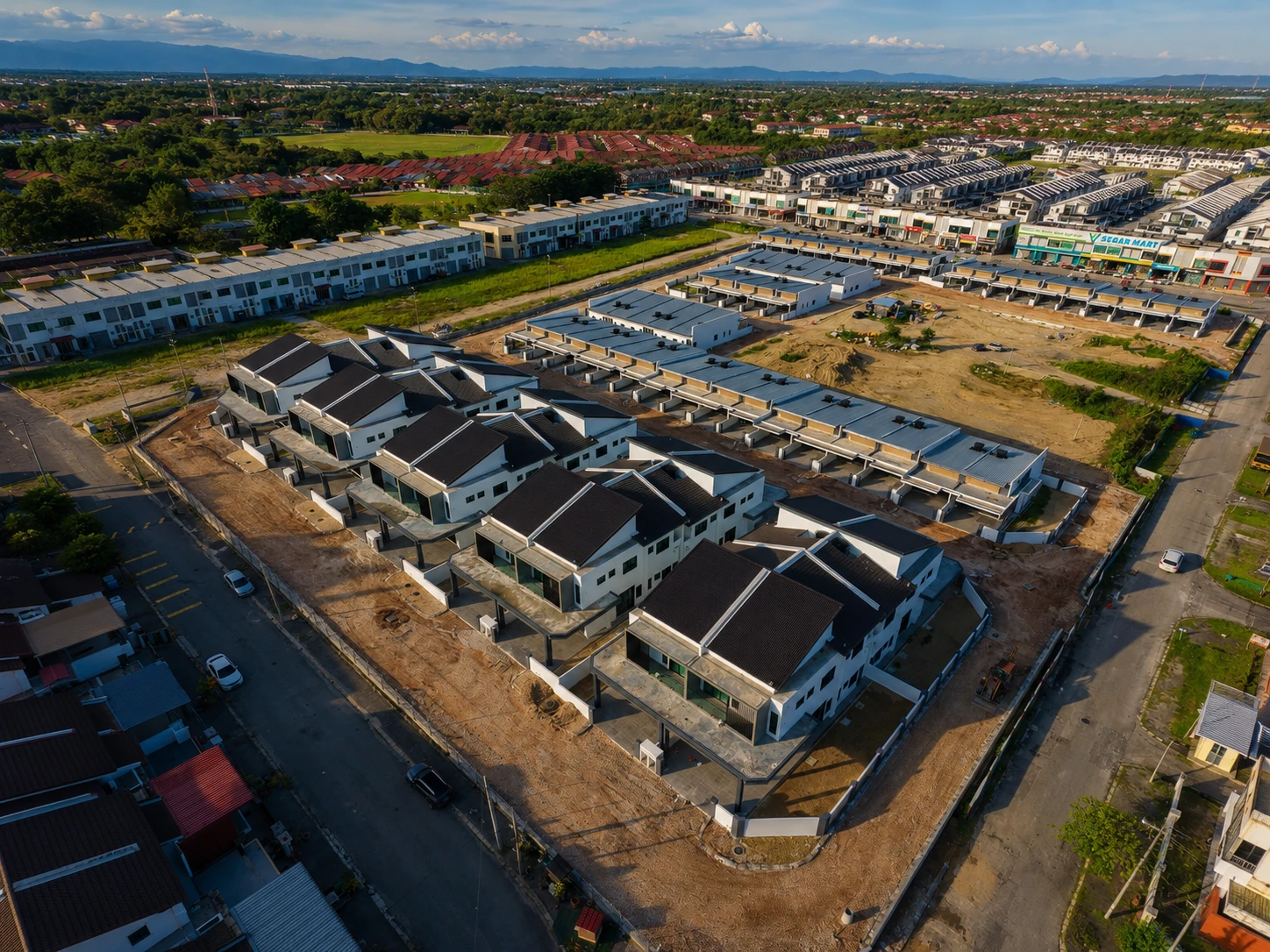 Aerial drone view of Taman Lapangan Irama under construction — completed terrace homes with dark roofs in the foreground, neighbouring developments and town in the background